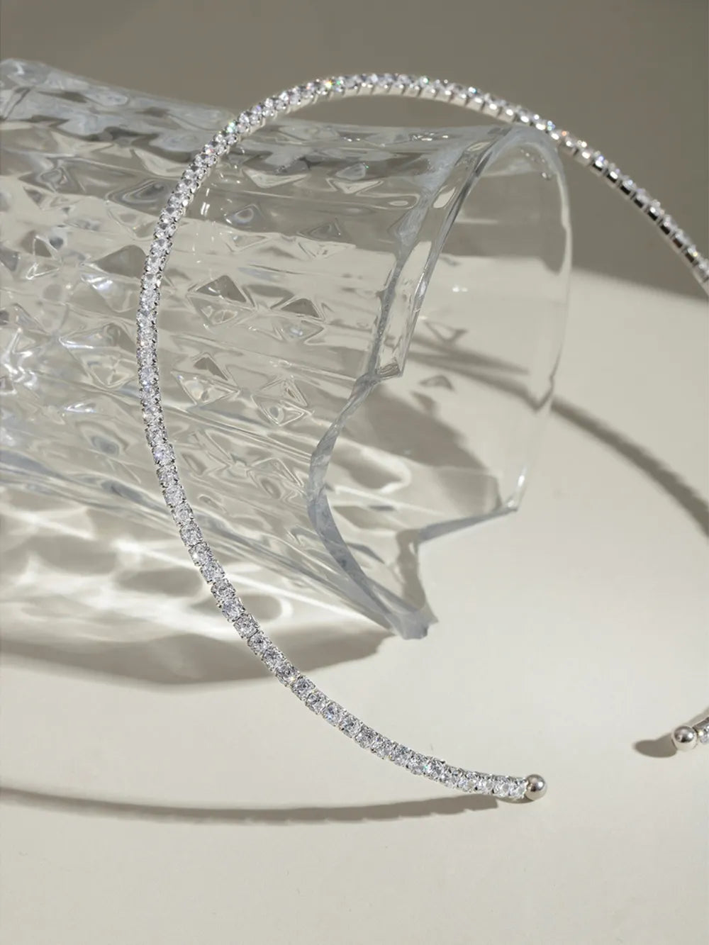 Silver headband with clear crystals on a clear stand against a neutral background