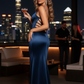Woman in a blue evening gown holding a drink on a rooftop with city skyline in the background