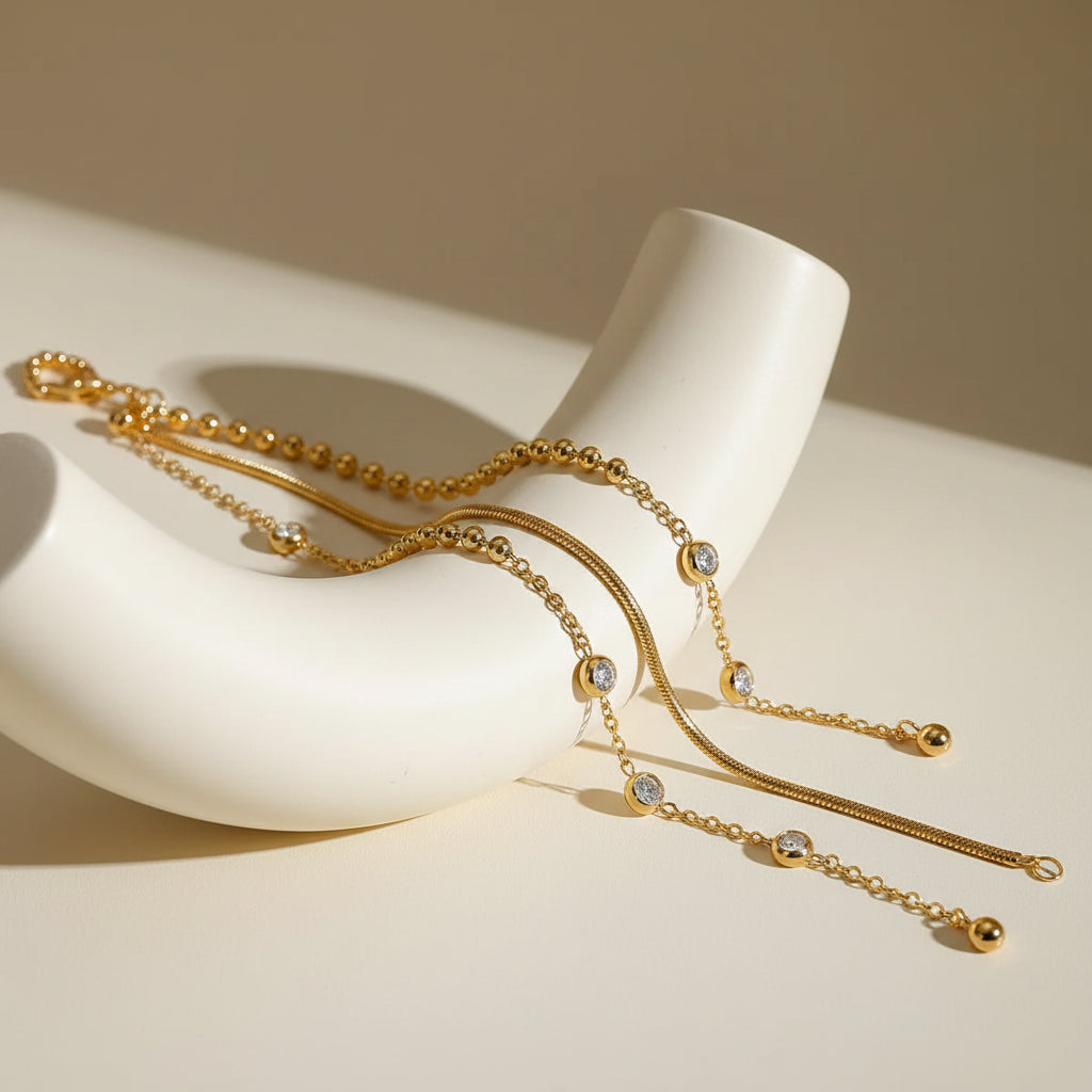 Gold necklaces on a textured surface with a glass and crystal dish in the background